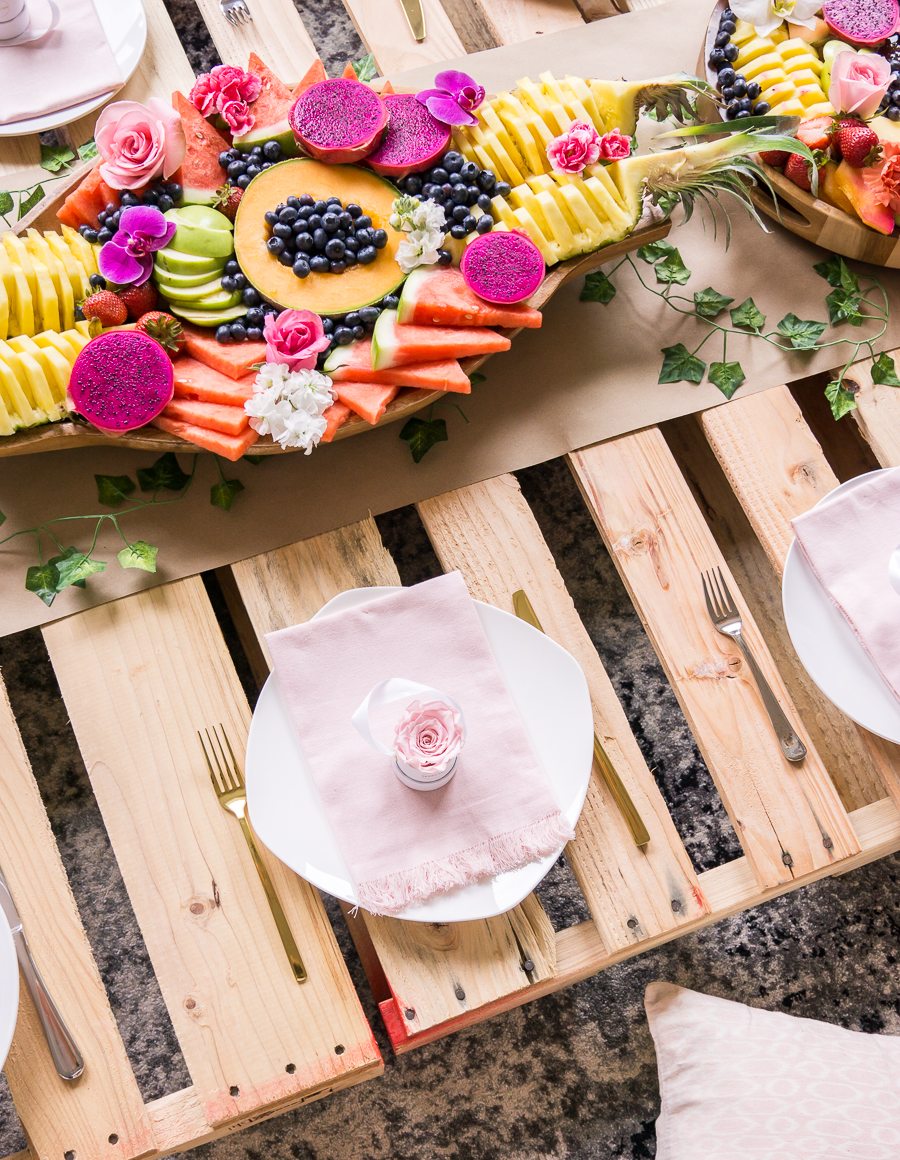 Picnic bridal shower with wood pallets, exotic fruit platters, table setting with gold flatware, mini rose boxes as party favors